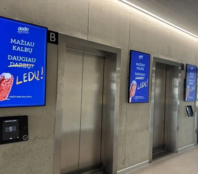 A portrait advertising screen next to the lifts in a business centre lobby
